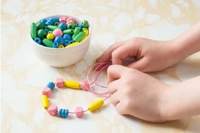 mains d'enfants réalisant un collier de perles